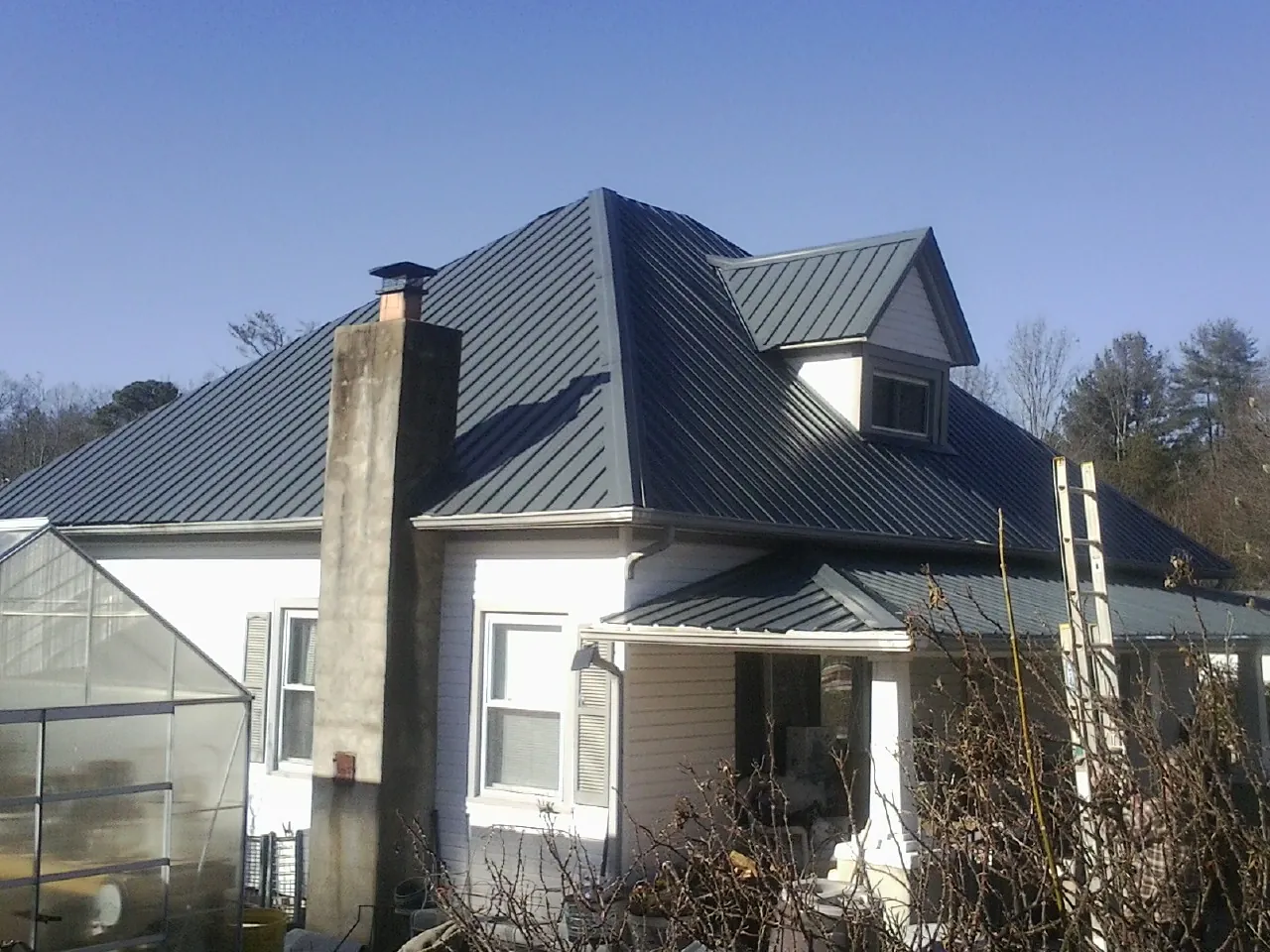 Dark blue standing seam metal roof on a white farmhouse with dormer — Slate & Tile Roof Repair by Roofing Brothers in Lolita