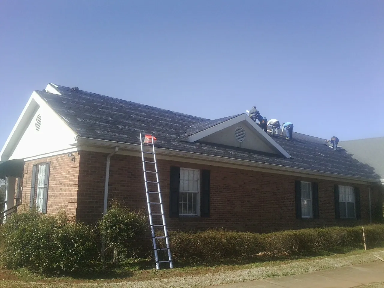 Crew tearing shingles off a brick ranch roof with a ladder set — Metal Roof Repair work by our crew in Lolita