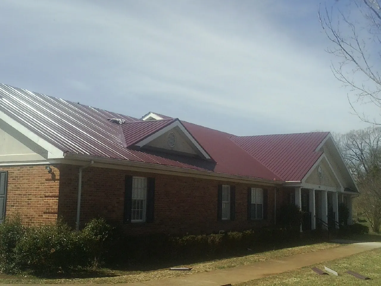 Red metal roof with gabled entries on a long brick building, from a Hail Damage Roof Repair job in Lolita