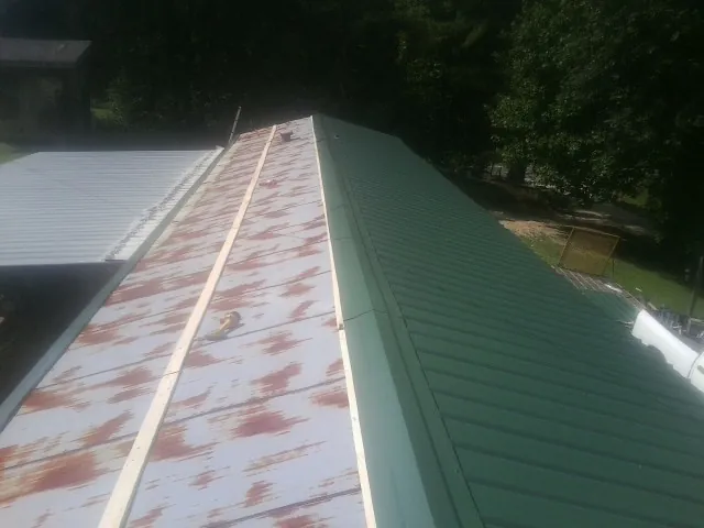 Old rusted panels beside newly installed green metal roofing — Wind Damage Roof Repair by Roofing Brothers in Lolita