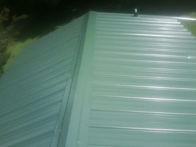 New green metal panels meeting at the ridge of a roof — Flat Roof Repair work by our crew in Lolita