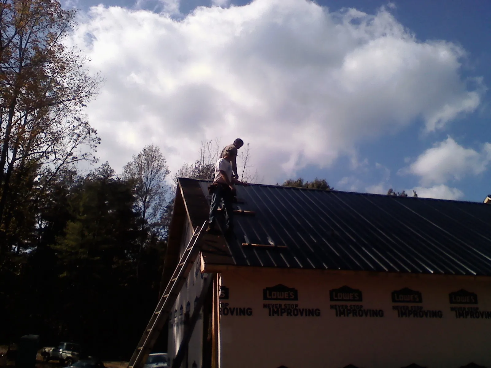 Roofer fastening dark metal panels high against a cloudy sky, from a Roof Inspection job in Lolita