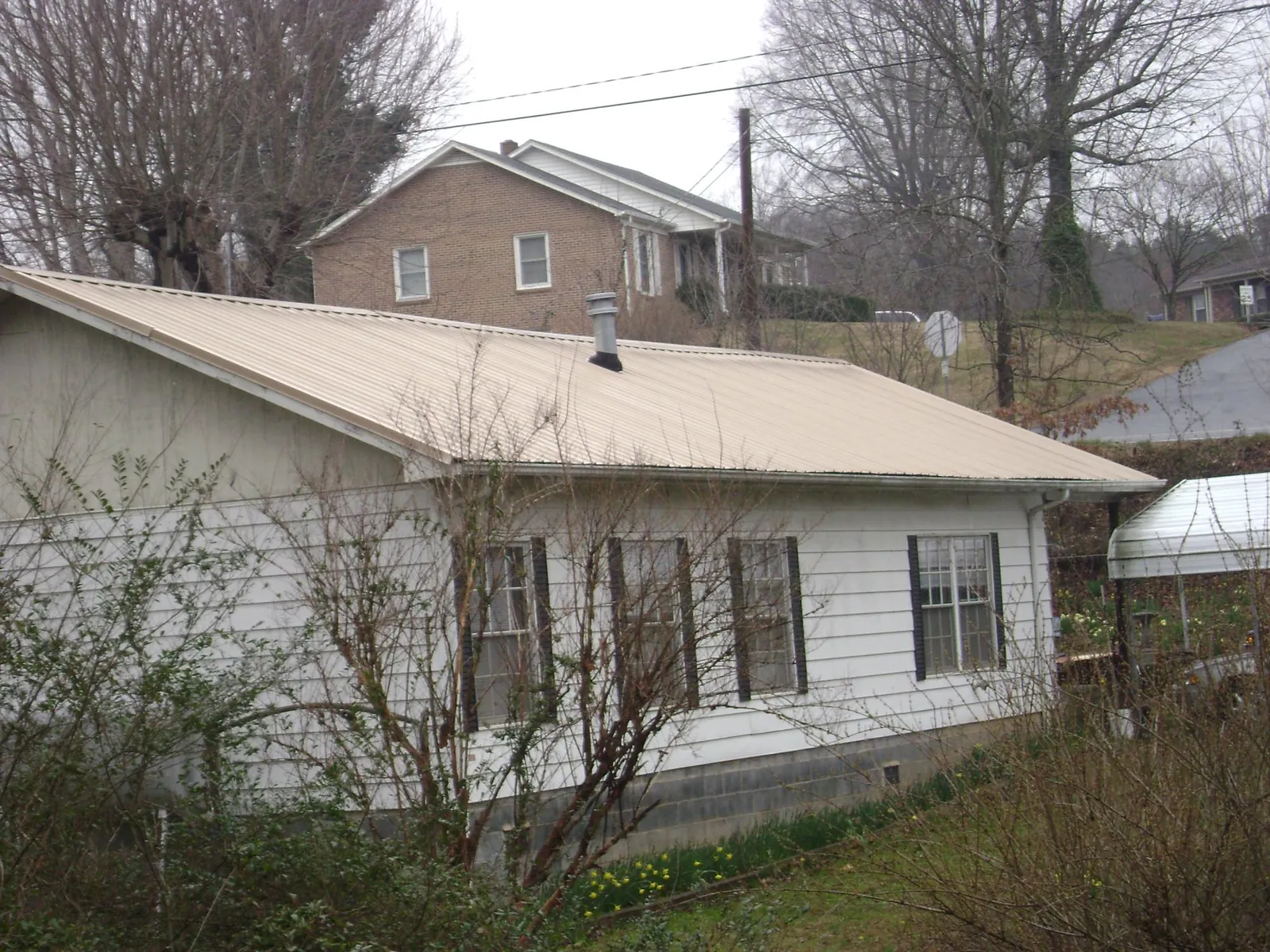 Tan metal roof on a white sided house set into a hillside — Commercial Roofing by Roofing Brothers in Lolita