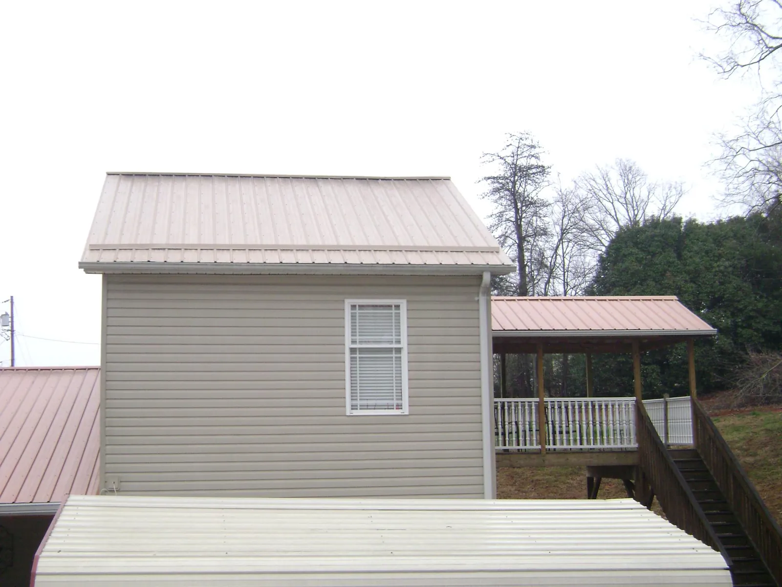 Tan metal roofs on a two story addition and attached porch, from a Roof Replacement job in Lolita